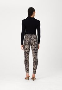 Top lungo a maniche nere a coste abbinato a leggings color beige con stampa leopardata nera e sandali con tacco a strisce marroni.