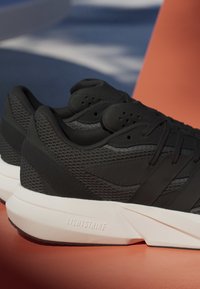 Čierne športové topánky s textúrovanou sieťovinou a hladkými časťami, s bielou podrážkou označenou "LIGHTSTRIKE." Šnúrky sú prevlečené cez čierne očká.