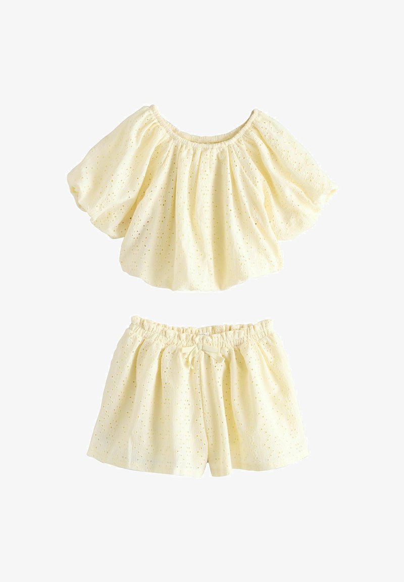 Ensemble deux pièces en tissu ajouré couleur crème, avec haut à manches courtes bouffantes et short taille élastique avec petit nœud à l'avant.