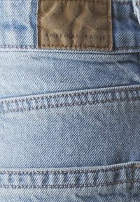 Šviesiai mėlynos džinsinės kelnės su tekstūruota ruda odine etikete "American Eagle". Yra siuvinėjimas ir galiniai kišenės.