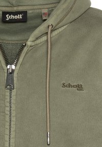 Olijf groene rits hoodie van gebreide stof, met een metalen rits en een geborduurd "Schott" logo in goud. Heeft trekkoorden met metalen uiteinden.