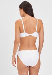 Weißes Wäscheset aus glattem Stoff, mit verstellbaren Trägern und gewelltem Saum an den Shorts, das ein nahtloses Design betont.