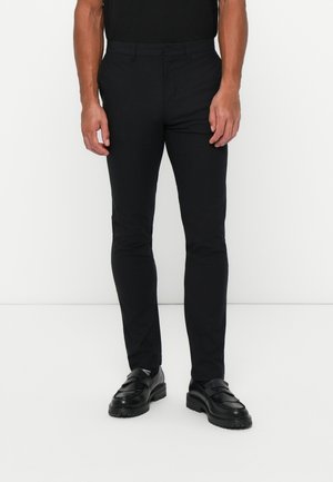 Black trousers with a slim fit, made of lightweight fabric. Feature a smooth texture, side pockets, and a zipper fly. Paired with black shoes.