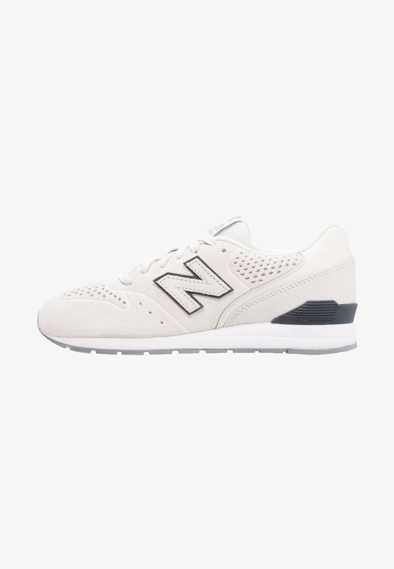 Chaussure de course New Balance blanche avec tige en daim, détails perforés et logo "N" noir sur le côté, sur fond blanc.