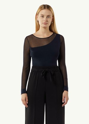 Marineblauw lange mouwen top met een doorschijnend gestreept paneel op één schouder, gecombineerd met hoge zwarte broeken met een strik taille en wijde pijpen.