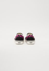 Des chaussures slip-on à carreaux noirs et roses avec un dessus en toile douce et une semelle en caoutchouc, présentant un logo sur le talon.
