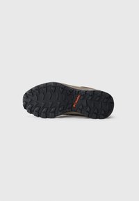 Black rubber outsole with deep treads for traction, featuring a brown upper with branding detail in orange. Flat, sturdy design for durability.