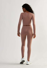 Sportowy zestaw w stonowanym różu, z prążkowaną teksturą, długimi rękawami oraz legginsami w wysokim stanie. W komplecie białe buty sportowe.