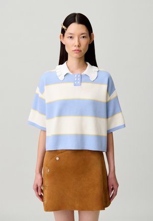 Haut crocheté aux rayures horizontales bleu clair, blanc et jaune ; doté d'un col à volants avec des boutons. Jupe en daim marron avec des accents à pression.