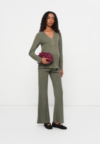 Set rib cu dungi de culoare verde măslină, cu mâneci lungi și decolteu în V. Pantaloni largi și evazați, asortați cu o poșetă burgundă și pantofi negri fără toc.