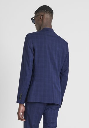Chaqueta de traje a cuadros azul marino con un corte moderno y ajustado, que presenta una abertura trasera y un detalle de cuatro botones en el puño. Diseño estructurado.