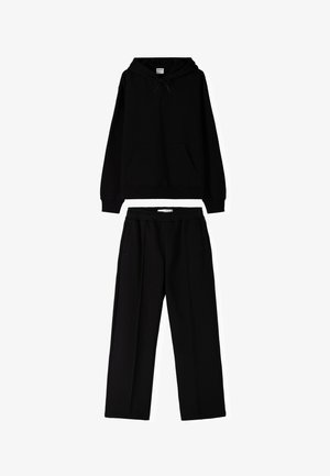 Schwarzer Hoodie mit einer Fronttasche und Kapuze mit Kordelzug, kombiniert mit passenden schwarzen weiten Hosen in lockerer Passform und seitlichen Taschen.