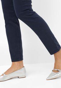 Stříbrné metalické baleríny s nízkým podpatkem a výřezem, které jsou spárovány s úzkými tmavě modrými kalhotami, a ukazují elegantní, moderní vzhled.