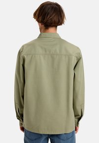 Green, long-sleeve shirt made of cotton. Features a standard collar and buttoned cuffs. Smooth texture with a relaxed fit, visible stitching details.