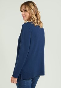 Navyblauer Pullover mit lockerem Schnitt, geripptem Saum und seitlichen Schlitzen. Weiche Textur, lange Ärmel und ein rundes Dekolleté.