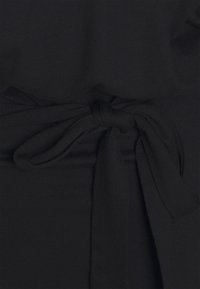 Černé šaty s jemnou texturou, které mají v pase uvázanou stuhu. Tkanina je hladká a šaty mají přiléhavý střih.