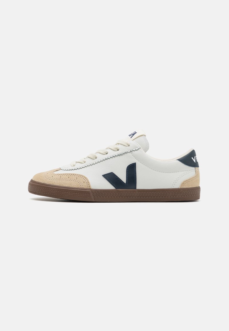Fehér sneaker bézs velúr részletekkel, barna gumitalppal és sötét tengerészkék logóval. Klasszikus fűzős kialakítással és texturált orr résszel rendelkezik.