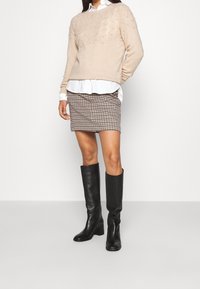 Beige gebreide trui met een textuurpatroon, witte overhemden met kraag, houndstooth mini-jurk en zwarte leren laarzen tot aan de knie.