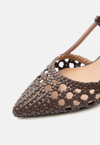 Καφέ πλεκτό δερμάτινο σανδάλι με μυτερή μύτη, σχεδιασμό πλέγματος και λουράκι στον αστράγαλο σε ανοιχτό φόντο.