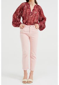 Punainen kuvioitu pusero, jossa on leveät hihat, yhdistettynä vaaleanpunaisiin suoriin farkkuihin ja neutraalinsävyisiin liukuviin sandaaleihin. Yksinkertainen muotoilu.