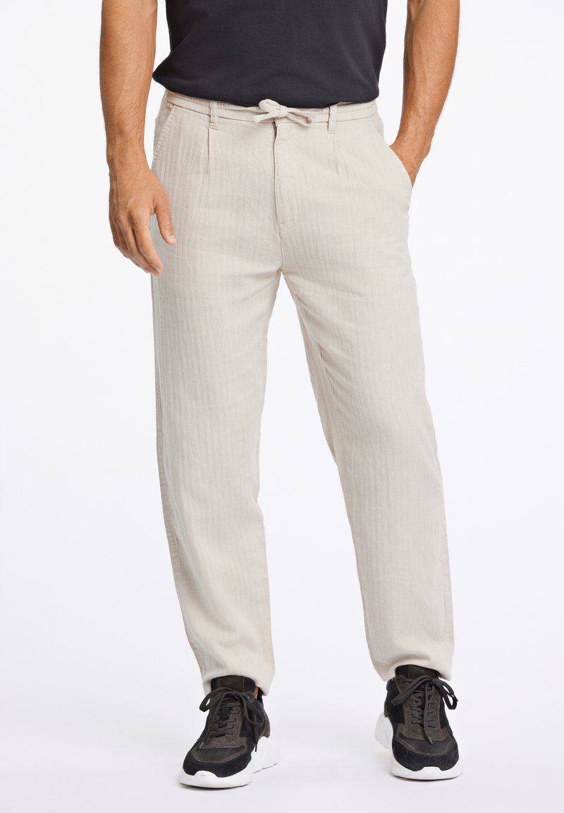 Beige broek van lichtgewicht stof, met een trekkoord in de taille, zijzakken en een losse pasvorm, gecombineerd met zwarte sneakers.