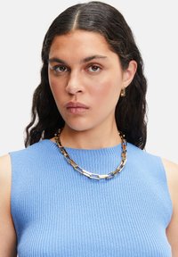 Collier en métal doré avec des maillons rectangulaires au fini texturé. Porté sur un haut sans manches côtelé bleu clair.