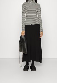 Gestreept zwart-wit coltopje met gerimpelde zoom, gecombineerd met een lange zwarte rok. Een zwarte tas met kettingriem en zwarte schoenen maken de look compleet.