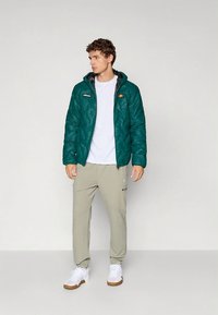 Turkusowa pikowana kurtka z kapturem, z logo na piersi, w połączeniu z jasnobeżowymi dresami i białymi tenisówkami. Gładka faktura i casualowy design.