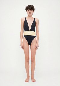 Svart ettstykke badedrakt med dyp V-hals, bredt gult midjebånd og høyt kutt på beina. Smooth stoff med minimalistisk design.