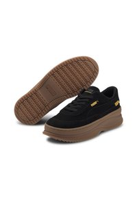 Baskets en suède noir avec une épaisse semelle en caoutchouc marron. Les caractéristiques comprennent un logo jaune sur le côté et une semelle extérieure texturée pour une meilleure adhérence.