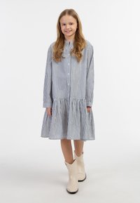 Stribet denim skjorte med lange ærmer, flagrende kant, blå og hvide striber, parret med lyse cowboystøvler.