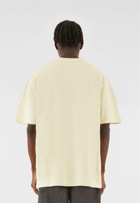 Světle žluté oversized tričko vyrobené z bavlny, s kulatým výstřihem a krátkými rukávy, s jednoduchým designem na zadní straně.