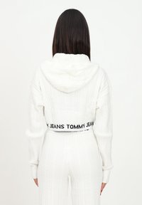 Bílá cropped mikina s pleteným vzorem, s kapucí a dlouhými rukávy, s černým elastickým pasem s logem "TOMMY JEANS".