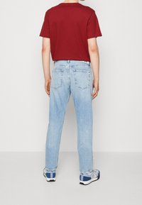 T-shirt rossa a maniche corte abbinata a jeans in denim azzurro chiaro. I jeans presentano una vestibilità dritta e tasche posteriori classiche con dettagli di cucitura.
