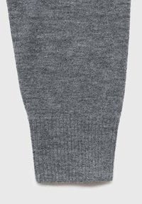 Gros plan d'une manche de pull gris tricoté avec un poignet côtelé sur un fond clair.