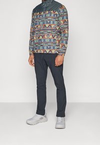 Multifarvet pullover med geometriske mønstre, med en mørkeblå skuldre og en høj krave. Sorte slim-fit bukser med grå sneakers.