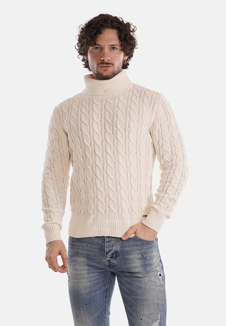 Maglione a collo alto lavorato a trecce di colore crema, con una consistenza spessa, polsini e orlo a coste, abbinato a jeans blu strappati.