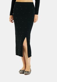 Falda de punto negro acanalada con cuentas decorativas plateadas, silueta ajustada y una abertura lateral. Combinada con bailarinas brillantes.