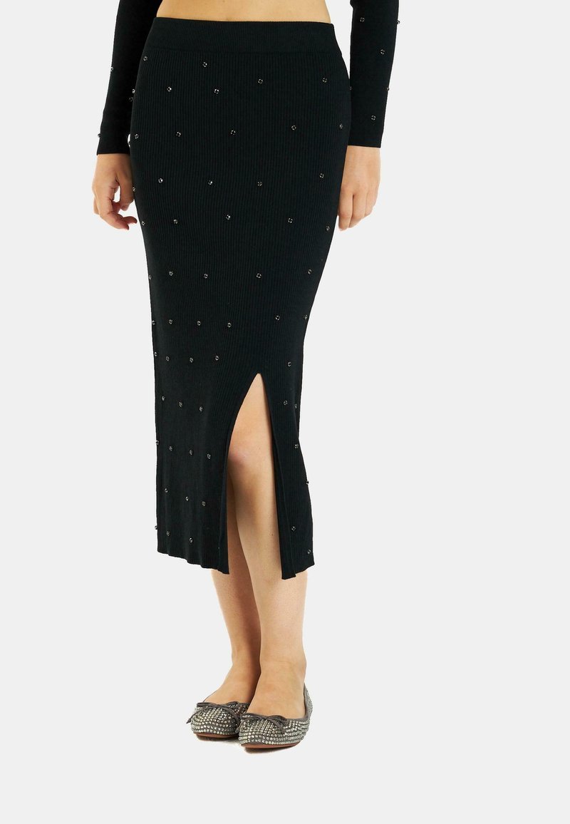 Falda de punto negro acanalada con cuentas decorativas plateadas, silueta ajustada y una abertura lateral. Combinada con bailarinas brillantes.