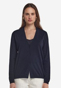 Marinblå cardigan i mjukt stickat tyg, med V-ringning, knappstängning, långa ärmar och ribbad kantdetalj.