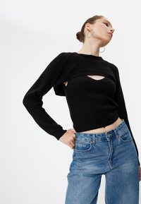 Schwarzer, gerippter, verkürzter Pullover mit einem Ausschnitt, kombiniert mit hochgeschnittenen blauen Jeans. Verfügt über lange Ärmel und ein enganliegendes Design.
