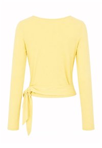 Haut jaune à manches longues style cache-cœur avec lien latéral à la taille, présenté sur fond blanc, vue de dos.