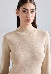 Pulover bej tricotat cu model cu dungi, guler înalt, mâneci lungi și textură netedă. Țesătura pare moale și se potriveste perfect.