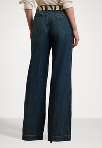 Mørkeblå vide jeans med en glat denimstruktur, der har subtile stikninger og et stribet bælte med et klassisk design.