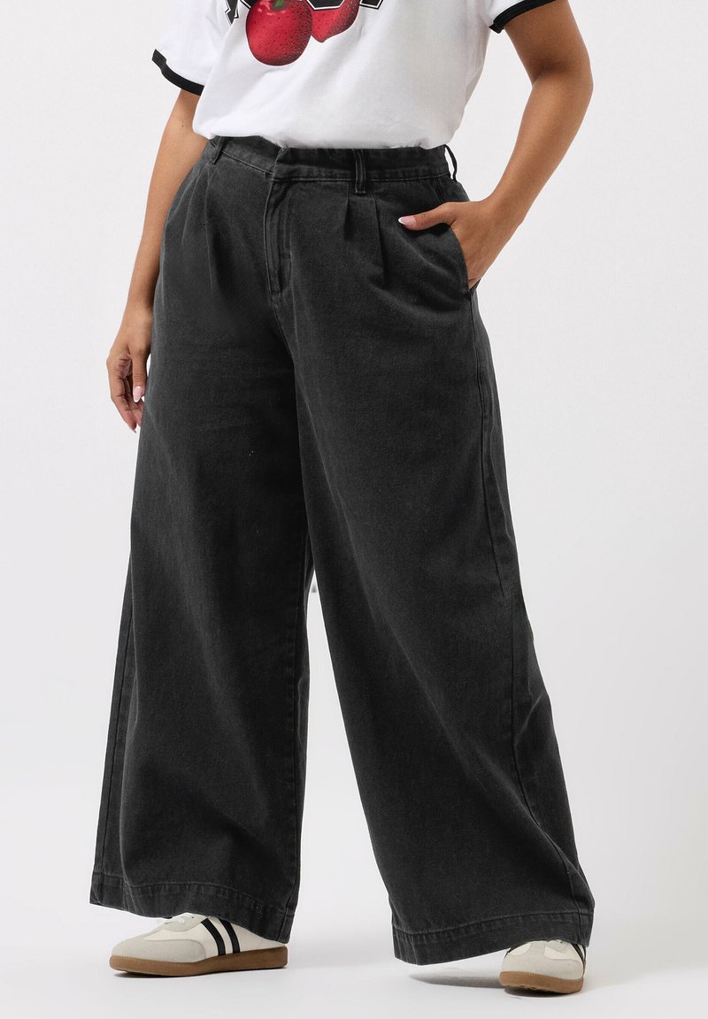 Mustat, leveät farkut korkealla vyötäröllä, laskosteet ja sivutaskut, yhdistettynä valkoiseen graafiseen t-paitaan ja kermaisiin kenkiin.