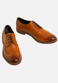 Bruine leren schoenen met een brogue-design, spitse neus, vijf vetersluiting en een contrasterende rubberen zool met een donkere rand.