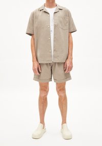 Camicia leggera beige a maniche corte con taschino sul petto, abbinata a pantaloni corti coordinati e zoccoli color crema. Fit semplice e rilassato con texture morbida.