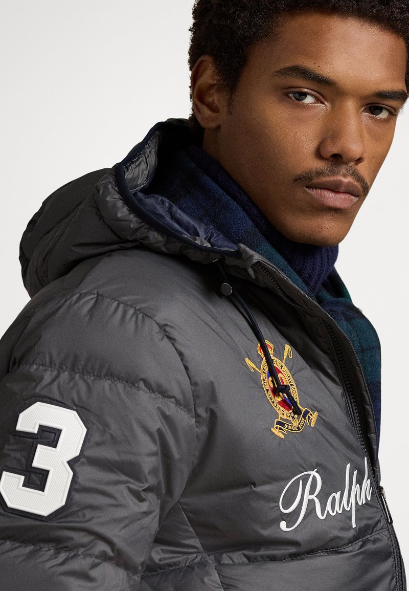 Doudoune grise avec capuche, arborant le chiffre 3 blanc et un logo brodé. En dessous, une écharpe à carreaux bleue et verte est visible.