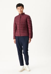 Chaqueta aislante burdeos con costuras horizontales, cremallera frontal y cuello alto; combinada con pantalones azul marino y zapatillas altas blancas.