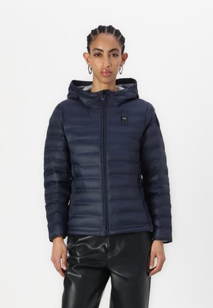 Doudoune marine avec capuche, design matelassé horizontal, fermeture éclair à l'avant et détail de logo. Portée sur un pantalon en cuir noir.